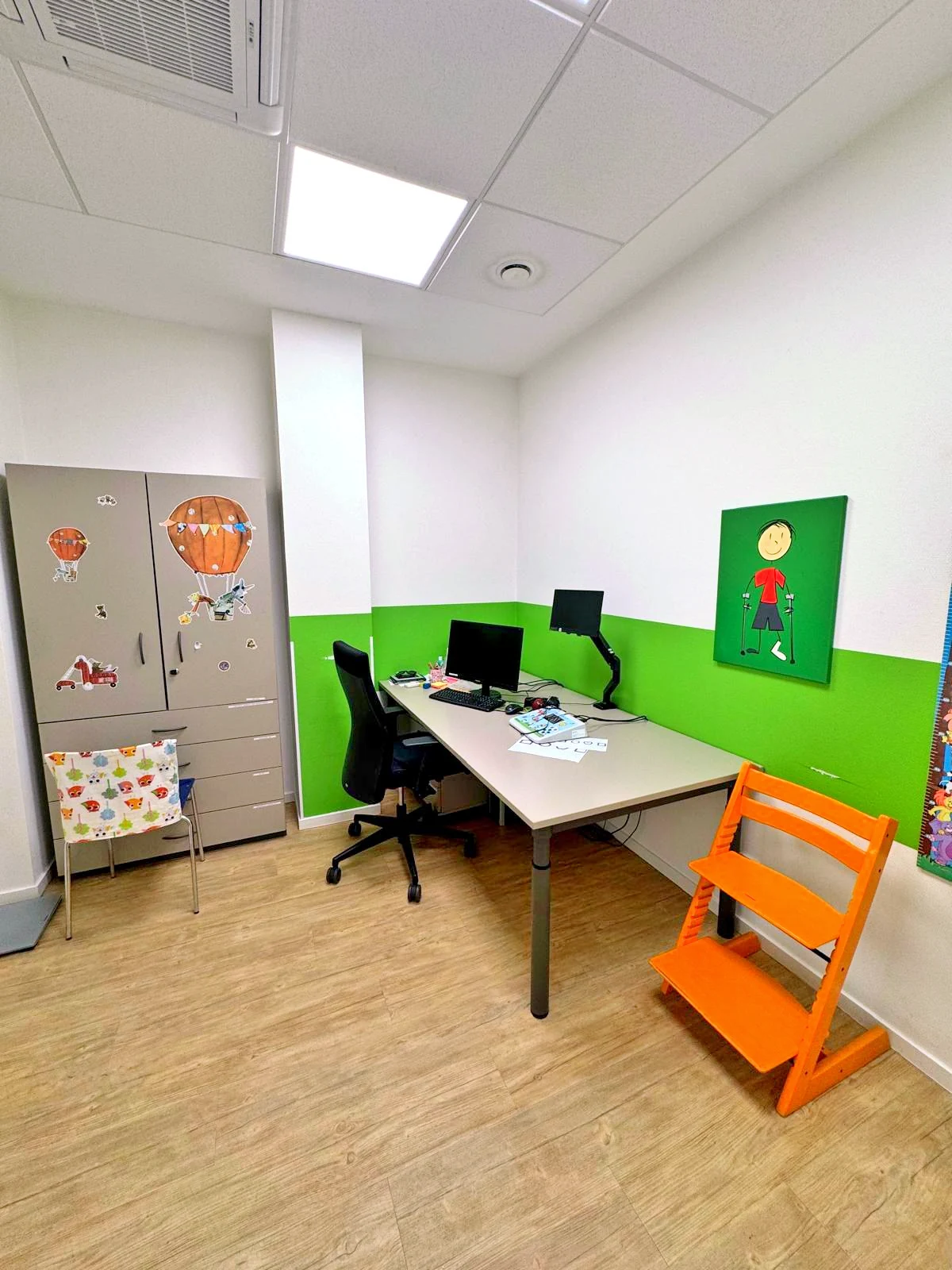 Sprechzimmer mit grüner Wandgestaltung, Schreibtisch und Kinderhochstuhl