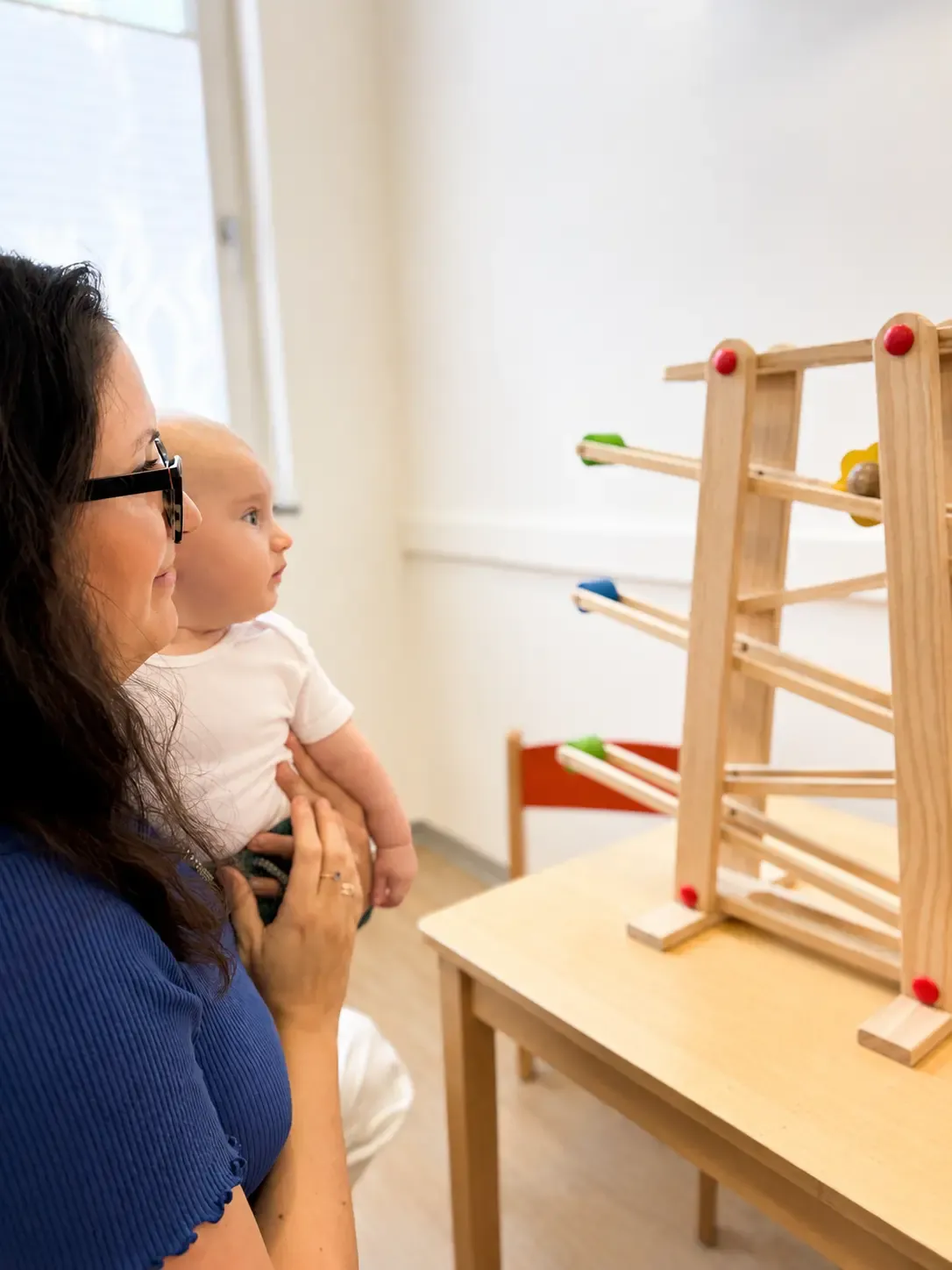 Mutter mit Baby vor einer Kugelbahn aus Holz im Wartebereich